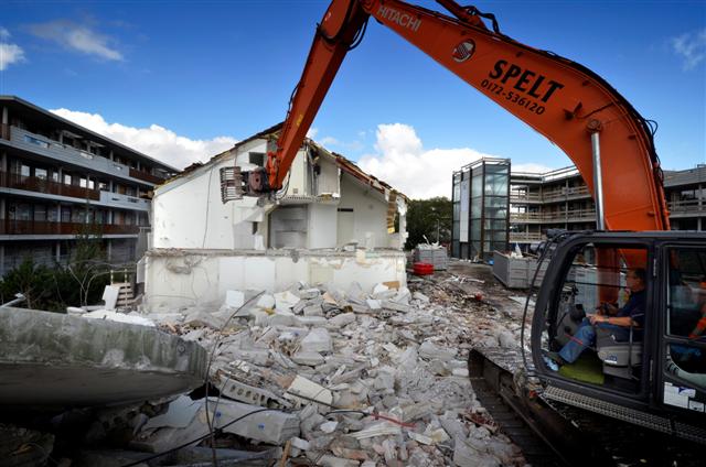 NIEUWKOOP - In Nieuwkoop sloopt een eenzame medewerker van Spelt uit Nieuwveen een oud blok woningen dat plaats gaat maken voor de laatste fase van nieuwbouwproject Klipperaak. Terwijl links al een deel van de door bouwbedrijf Vink+Veenman gebouwde woningen bewoond zijn, wordt rechts een nieuw blok binnenkort opgeleverd. In opdracht van Woning Stichting Nieuwkoop moeten uiteindelijk vijf vijf bouwblokken verrijzen die ruimte gaan bieden aan 58 levensloopbestendige appartementen voor senioren. Terwijl vroeger de woningen grotendeels met de hand gesloopt werden, trekt de machinist
