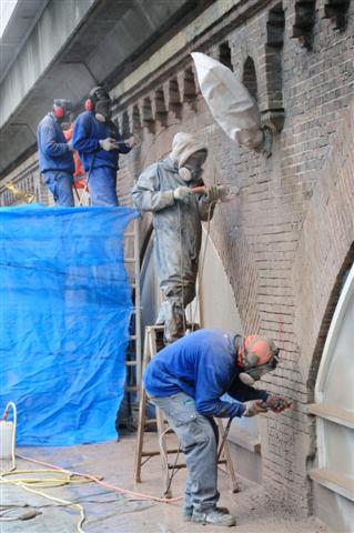 Foto Ronald Bakker
De gevel van Tussen de Bogen wordt opgeknapt. De voegen worden opnieuw gedaan, kapotte bakstenen vervangen en opnieuw gevoegd. Tussen de Bogen is de naam voor ateliers en kantoren die gevestigd zijn onder het NS spoor op de Amsterdasme Haarlemmer Houttuinen tussen het Haarlemmerplein en de Buiten Oranjestraat. Aannemer is de Van Ieperen Groep uit IJsselstein.