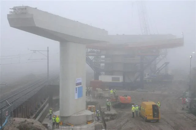 Foto Ronald Bakker
Medewerkers van aannemersbedrijf Heijmans draaien dinsdagmorgen in de mist een dwarsligger voor de toekomstige Westrandweg op zijn plek. Een deel van de dwarsligger hangt over een goederenspoorbaan in Westpoort.