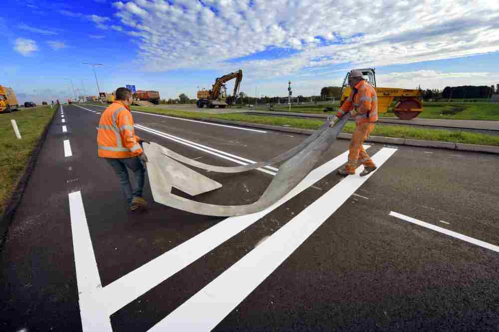 GELDERMALSEN - Op de provinciale weg N237 brengen medewerkers van Heijmans Wegenbouw pijlen aan op het nog warme asfalt tijdens wegwerkwerkzaaamheden op de kruising bij de afslag A2. Hoewel het werk er schijnbaar ongevaarlijk uitziet, werkt de figuratieploeg met gloeiend hete wegverf die meer dan kokend heet is: 180 graden Celcius. De mannen werken daarom meestal met lange mouwen en dragen handschoenen met leren stukken. Omdat de wagen nog niet op het warme asfalt kan rijden, moeten de sjablonen zelf af en toe naar de juiste plaats versleept worden. Behalve het vervangen van het wegdijk, en markeren met strepen, zijn tevens nieuwe detectielussen aangebracht. COPYRIGHT TON BORSBOOM
