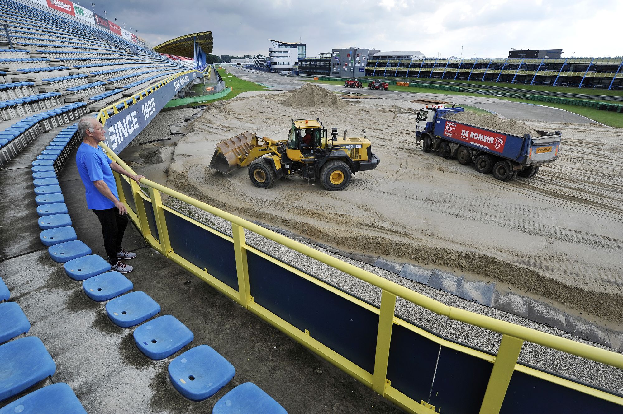 Het TT-circuit in Assen wordt een grote zandbak. Waar anders snelle motoren over het asfalt scheuren, rijden nu vrachtwagens af en aan met zand. Vier dagen lang is aannemer De Romein uit Veendam in touw. In totaal 24.000 kuub zand is nodig voor het circuit, waarop komend weekend de wereldkampioenschappen motorcross worden gehouden. Het parcours ligt normaliter in de bossen, waar geen tribunes zijn. Het TT-circuit heeft voldoende zitplaatsen voor enkele duizenden belangstellenden. Het zand komt van Defensie, die vlakbij het TT-circuit een zanddepot heeft. ,,Logistiek gezien is het bijna onmogelijk, dat zeggen collega's ook, maar het is fantastisch om te doen'', vertet Harm Jan Haan van De Romein. Acht vrachtwagens, shovels, rupskranen en mobiele kranen worden ingezet op het 1,5 kilometer lange traject te prepareren. In totaal worden twaalfhonderd vrachtwagenladingen opgehaald.