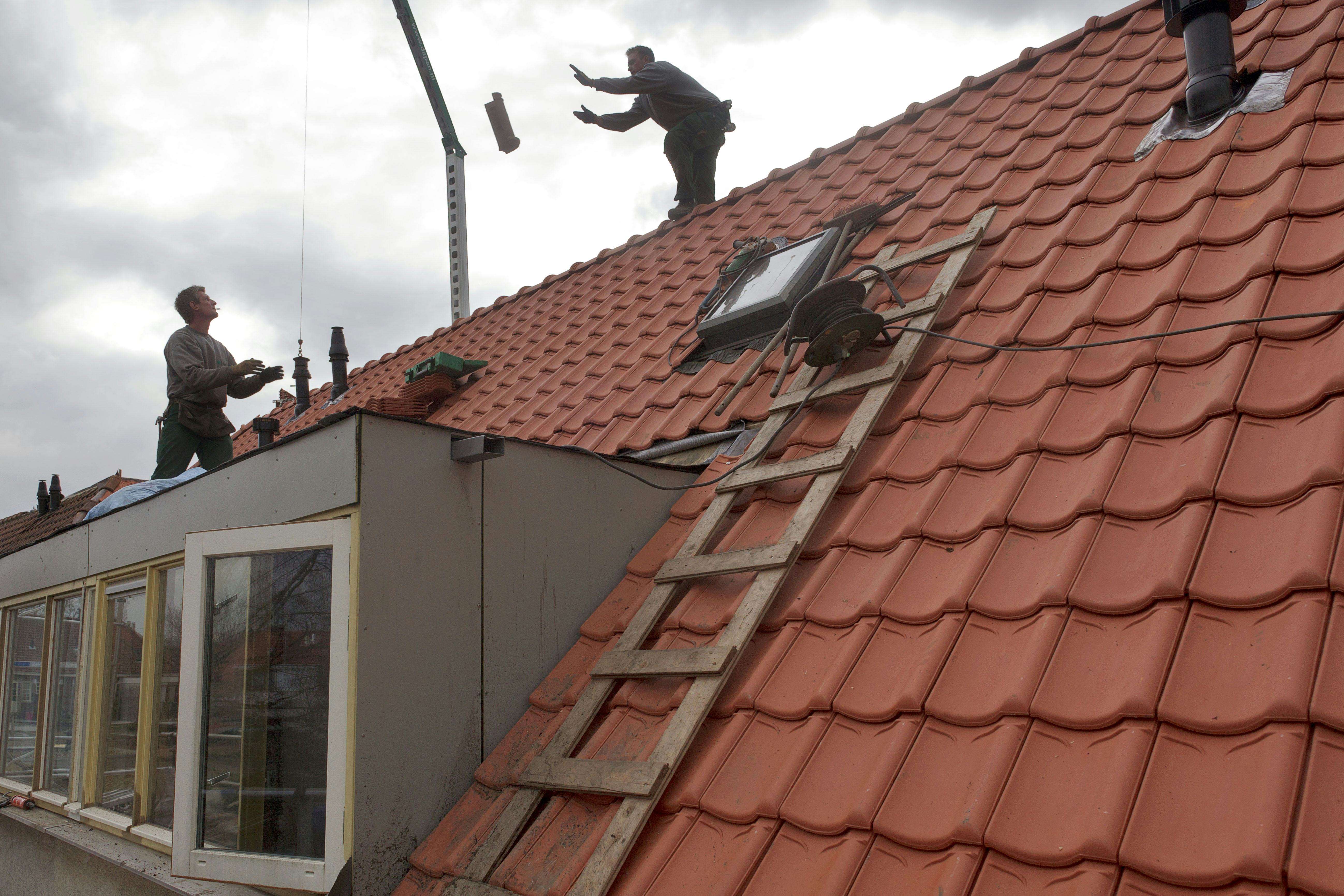 Nederland, Tilburg, 9 maart 2012
dakdekkers aan het werk in 1 van de te renoveren huizen. Oude huizen worden voorzien van nieuwe daken met rode dakpannen. Vier aannemers en een woningcorporatie geven in Tilburg inhoud aan het begrip ketensamenwerking. Niet de directeuren, maar de projectleiders en de werkvoorbereiders bepalen wie wat doet bij de renovatie van 178 arbeiderswoningen in de wijk Loven. Het blijkt dat openheid en onderling vertrouwen kostenbesparend en kwaliteitsverhogend werken.
Foto: Dolph Cantrijn/Hollandse Hoogte