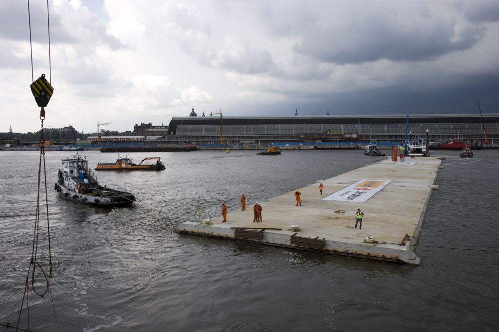 Nederland, Amsterdam,juli 2007
Aanleg Noord-Zuidlijn van de Amsterdamse Metro.
Bouwdok Sixhaven.
Twee reusachtige tunneldelen van de Noord/Zuidlijn, die in de loop van 2010 onder het IJ en onder het Centraal Station komen te liggen, worden vanuit het bouwdok naast de Sixhaven over het IJ weggesleept naar een tijdelijke parkeerplaats  in de Suezhaven (Westelijk Havengebied). Het tunneldeel dat in 2010 onder het Centraal Station zal worden afgezonken omvat het gehele toekomstige metrostation Centraal Station.
Dit tunneldeel wordt hier uit het bouwdok weggesleept. Vier sleepboten manoeuvreren het 22.000 ton wegende gevaarte in positie en verslepen het naar de Suezhaven. Op het moment dat het tunneldeel uit het bouwdok is gesleept en overdwars in het IJ ligt, wordt al het scheepvaartverkeer op het IJ tijdelijk stilgelegd. Op dinsdag 10 juli wordt het tweede tunneldeel weggesleept.
Het tunneldeel is nu in zijn geheel uit het dok gesleept. Op de achtergrond komt een onweersbui aanzetten.
Het gereedkomen van de tunneldelen en het transport naar de Suezhaven vormen een mijlpaal in de aanleg van de Noord/Zuidlijn. De in totaal vier tunneldelen die in 2010 onder het IJ en het Centraal Station komen te liggen zijn nu klaar en liggen geparkeerd in de Suezhaven. In juni vorig jaar werden de eerste twee tunneldelen uit het bouwdok weggesleept.
Foto: Gé Dubbelman/Hollandse Hoogte
Opdrachtnummer: D10023