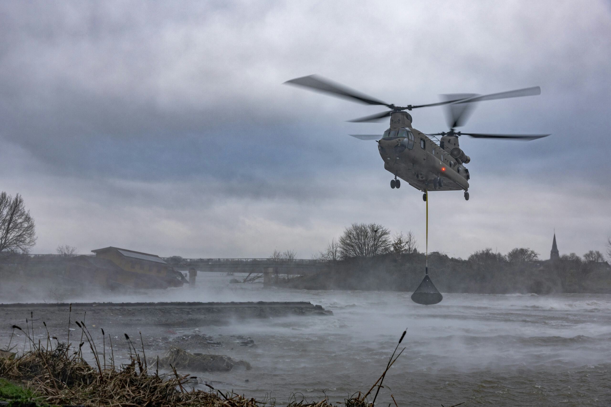 Een Chinook-helikopter dropt een net met stenen op de bezweken overlaatdam. Foto: Defensie.
