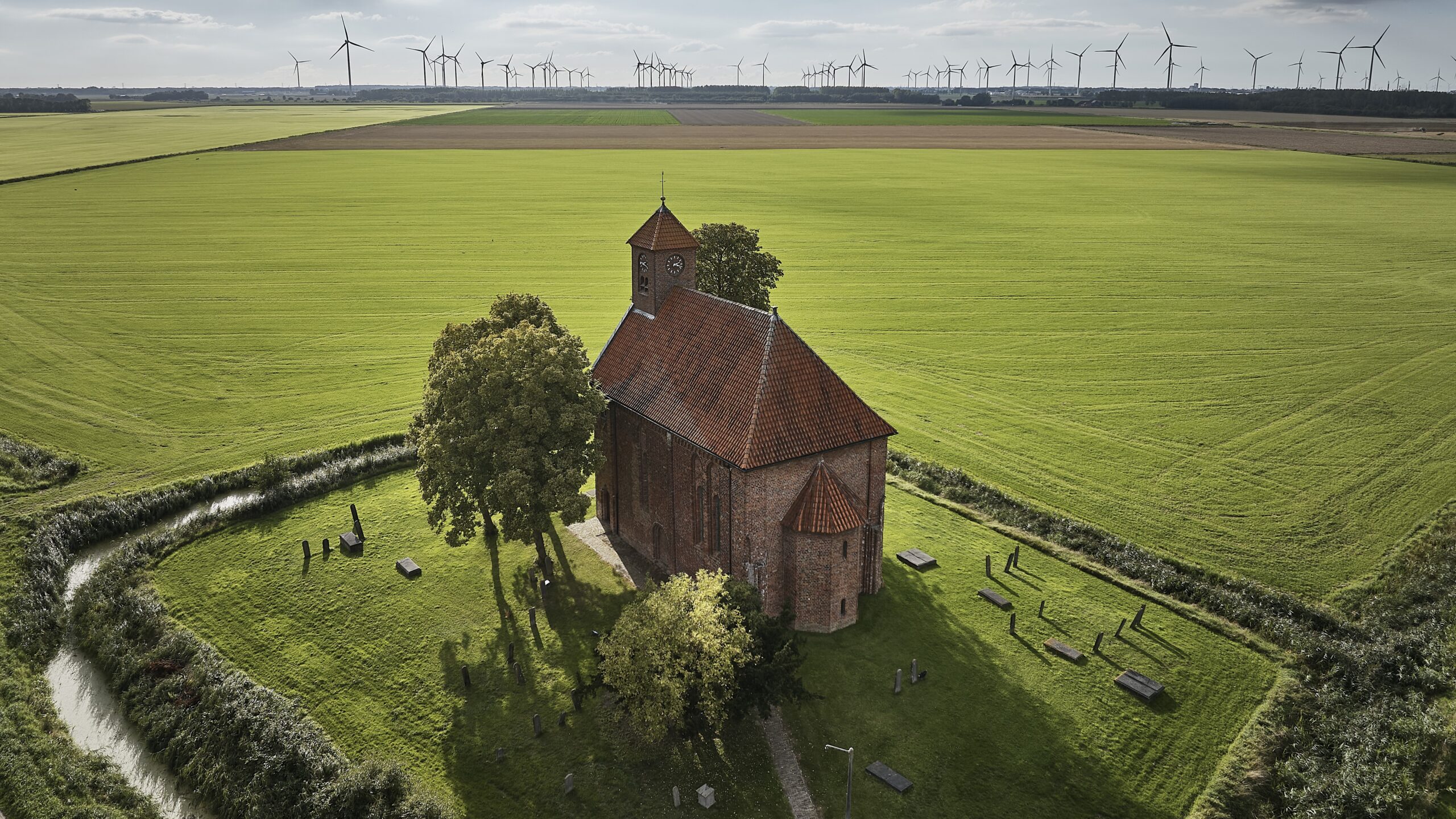 Een kerk in de Groningse gemeente Eemsmond, met in de verte het windpark van Delfzijl. Foto: ANP/HH/Siebe Swart