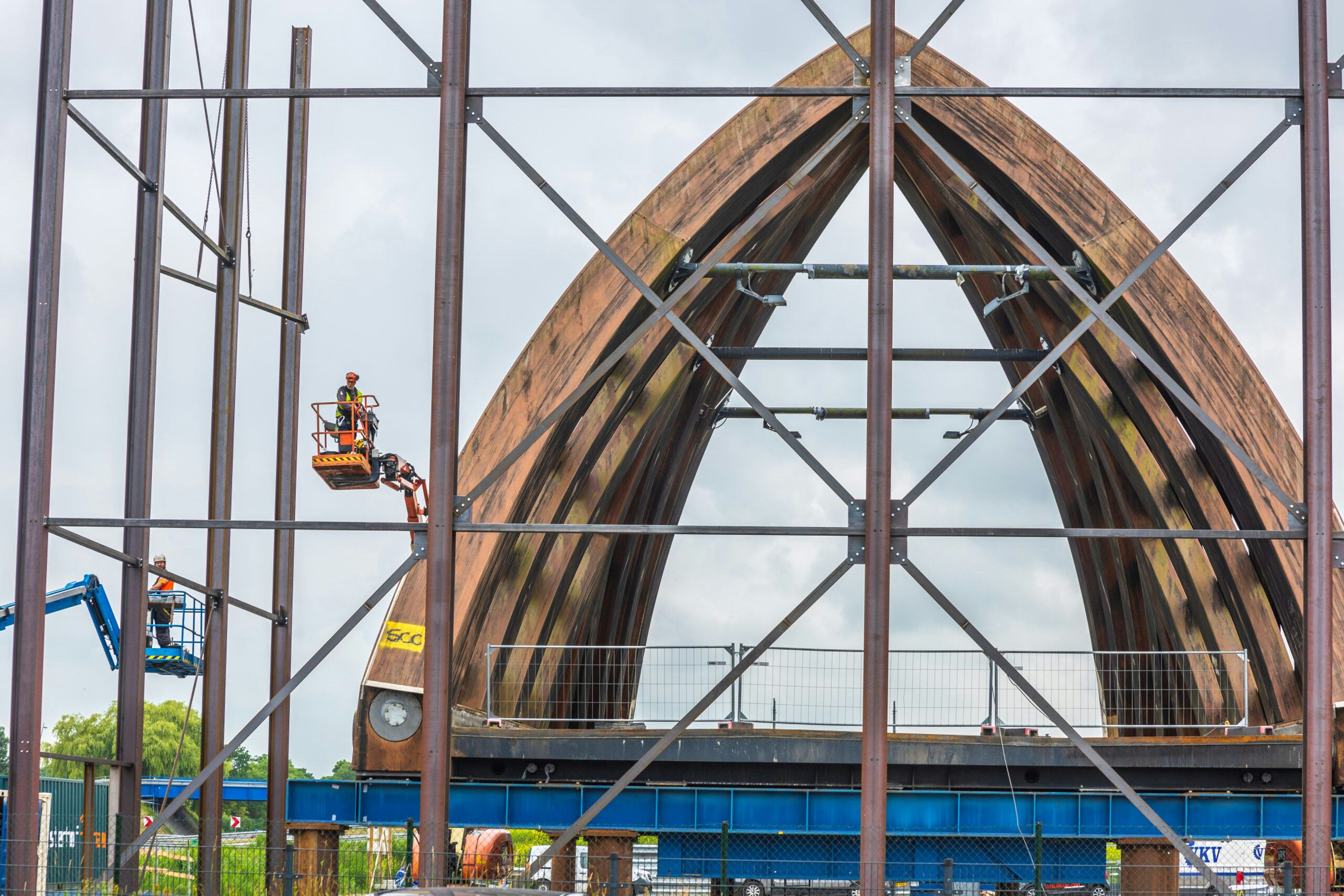 Aannemer Oosterhof Holman bouwt pal langs de A7 een grote loods. Daarbinnen wordt de Krúsrakbrug opnieuw geconserveerd. De houten brug over de snelweg is daarvoor twee maanden terug al van zijn landhoofden getild en een stukje verderop neergelegd. Foto: Niels de Vries