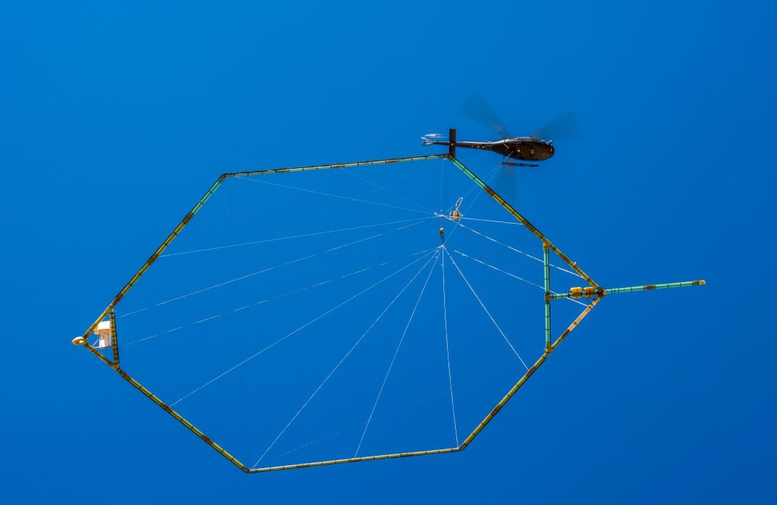 De enorme hoepel onder de helikopter bevat een spoel die elektromagnetische straling van verschillende frequenties de bodem in stuurt en na reflectie weer opvangt. Foto:  SkyTEM