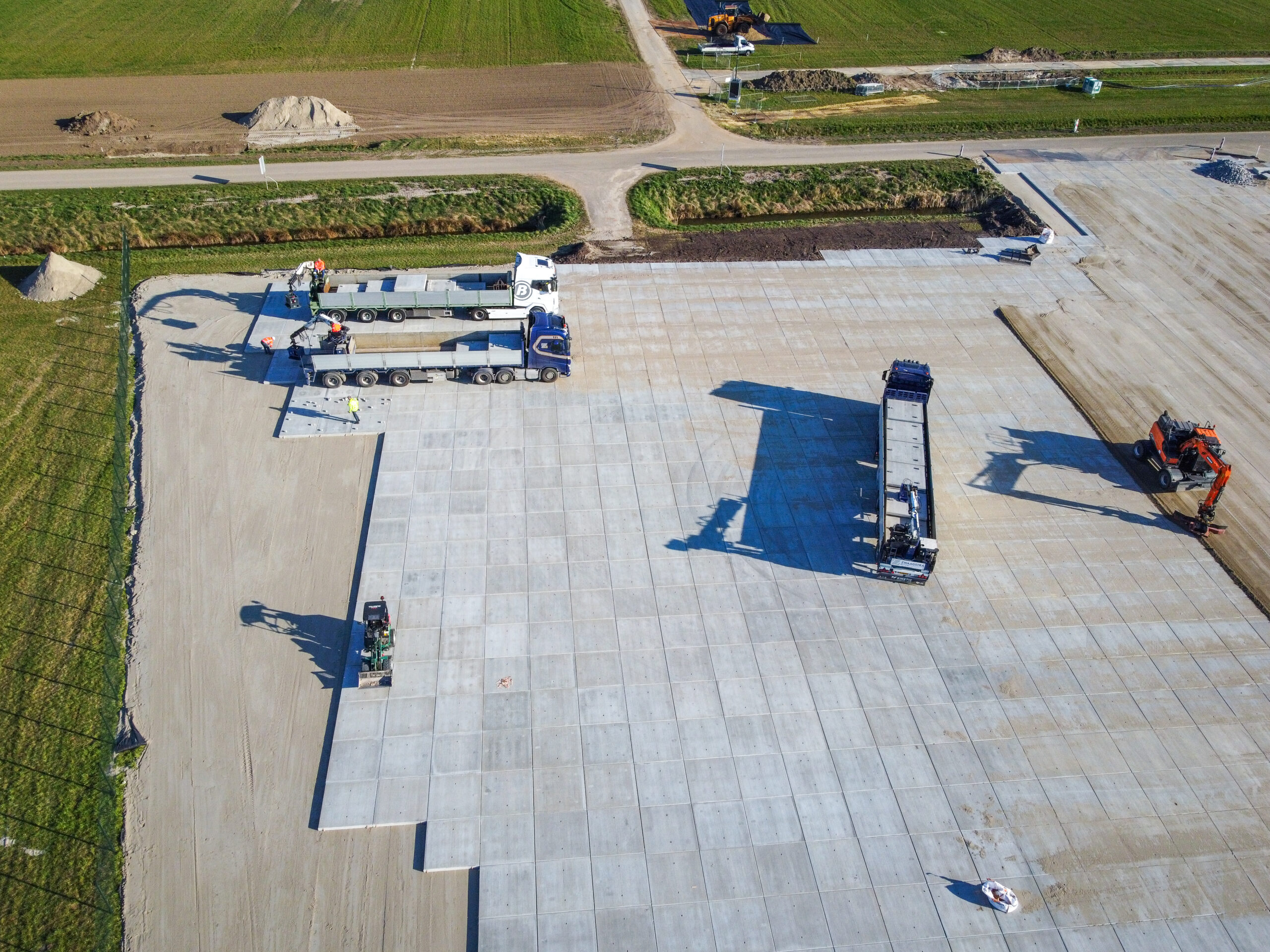 Direct vanaf de vrachtauto’s worden de betonplaten nauwkeurig geplaatst bij de opslaglocatie van Belectric. Project: Zonnepark Eekerpolder.